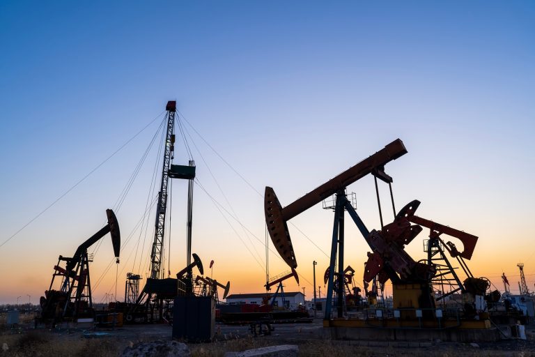 Silhouetted oil pumpjacks at sunset over an energy field.