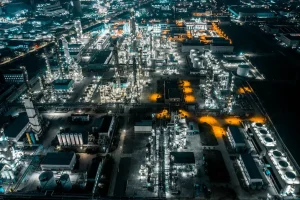 Aerial view of an illuminated oil refinery at night, showcasing its complex structures and vibrant lights