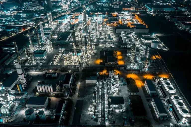 Aerial view of an illuminated oil refinery at night, showcasing its complex structures and vibrant lights