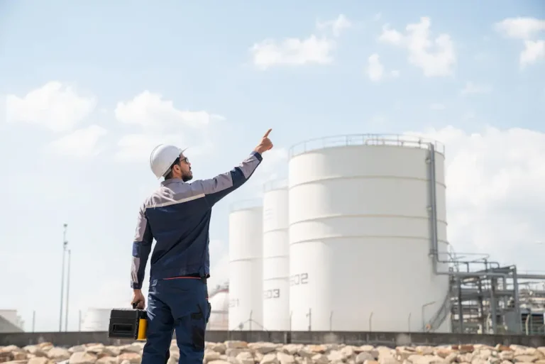 A man in a hard hat points at a large oil refinery
