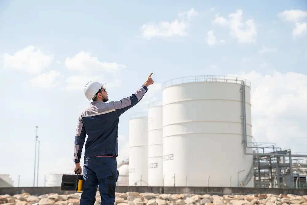 A man in a hard hat points at a large oil refinery