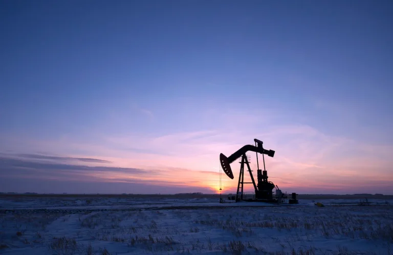 An oil drilling rig and pumpjack on a flat plain in oil fields at sunset.